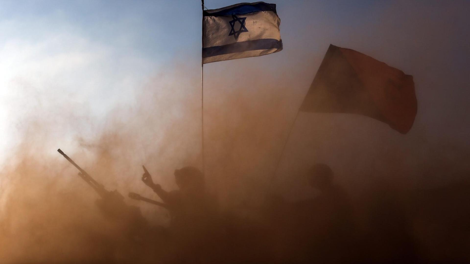 In einer Staubwolke sind die Umrisse eines Panzers und eines Soldaten zu sehen. Darüber weht die israelische Flagge. In einer Staubwolke sind die Umrisse eines Panzers und eines Soldaten zu sehen. Darüber weht die israelische Flagge.