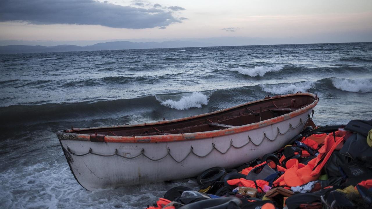 Am Strand der griechischen Insel Lesbos liegen ein Holzboot und viele Rettungswesten