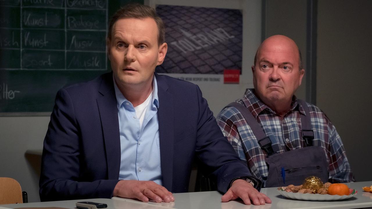 "Das Unwort": Direktor Stege (Devid Striesow) und Hausmeister Eichmann (Florian Martens) sitzen nebeneinander an einem der Schultische. Vor ihnen steht ein Teller mit Leckereien, im Hintergrund sind eine Kreidetafel sowie ein Plakat mit der Aufschrift "Toleranz" zu erkennen. Stege legt beide Hände flach auf den Tisch und schaut entsetzt. Eichmann blickt mürrisch in dieselbe Richtung wie Stege. "Das Unwort": Direktor Stege (Devid Striesow) und Hausmeister Eichmann (Florian Martens) sitzen nebeneinander an einem der Schultische. Vor ihnen steht ein Teller mit Leckereien, im Hintergrund sind eine Kreidetafel sowie ein Plakat mit der Aufschrift "Toleranz" zu erkennen. Stege legt beide Hände flach auf den Tisch und schaut entsetzt. Eichmann blickt mürrisch in dieselbe Richtung wie Stege.