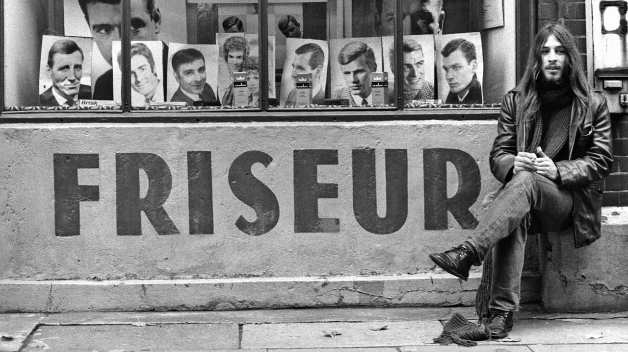 Ganz sicher kein Kunde: Ein langhaariger junger Mann sitzt vor einem Friseursalon in der Langen Straße auf St. Pauli in den 1960er-Jahren