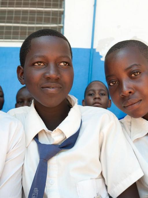 Portrait von drei Mädchen im Teenageralter in einer Schule in Tansania. Sie tragen Schuluniform, weiße Blusen und blaue Krawatten, und lächeln in die Kamera.