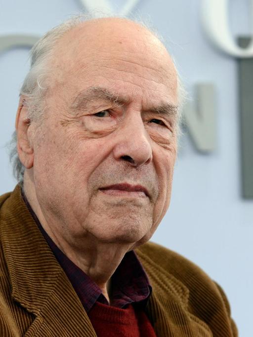 Der 84-jährige Autor Karl-Heinz Bohrer blickt in die Kamera. Er trägt ein braunes Cordsakko und im Hintergrund ist eine Buchstaben-Dekoration der Leipziger Buchmesse zu sehen.