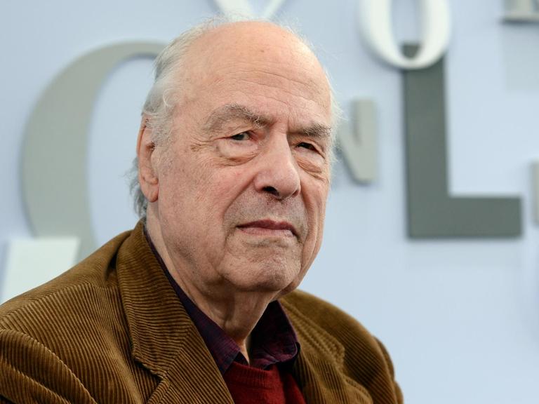Der 84-jährige Autor Karl-Heinz Bohrer blickt in die Kamera. Er trägt ein braunes Cordsakko und im Hintergrund ist eine Buchstaben-Dekoration der Leipziger Buchmesse zu sehen.