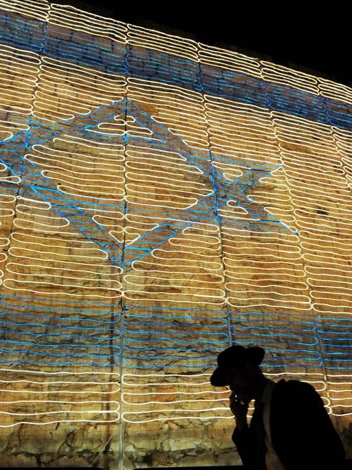 Es ist der 9. Mai 2011, der Unabhängigkeitstag in Israel und ein orthodoxer Jude mit Hut telefoniert und blickt dabei auf den Boden, im Hintergrund die israelische Flagge, bestehend aus Lichterketten in der alten Stadt Jerusalem. Sie feiern den 63. Geburtstag des Beginns eines jüdischen Staates.