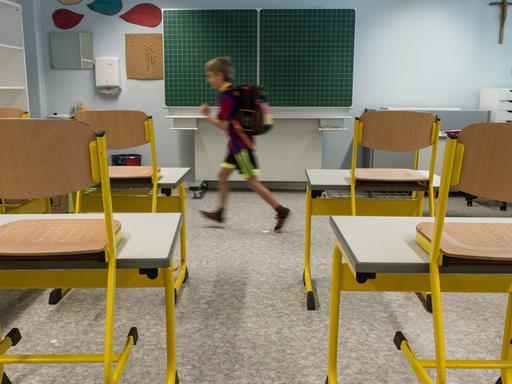 Leeres Klassenzimmer mit hochgestellten Stühlen, aus dem ein Drittklässler läuft.
