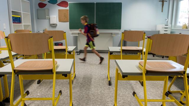 Leeres Klassenzimmer mit hochgestellten Stühlen, aus dem ein Drittklässler läuft.