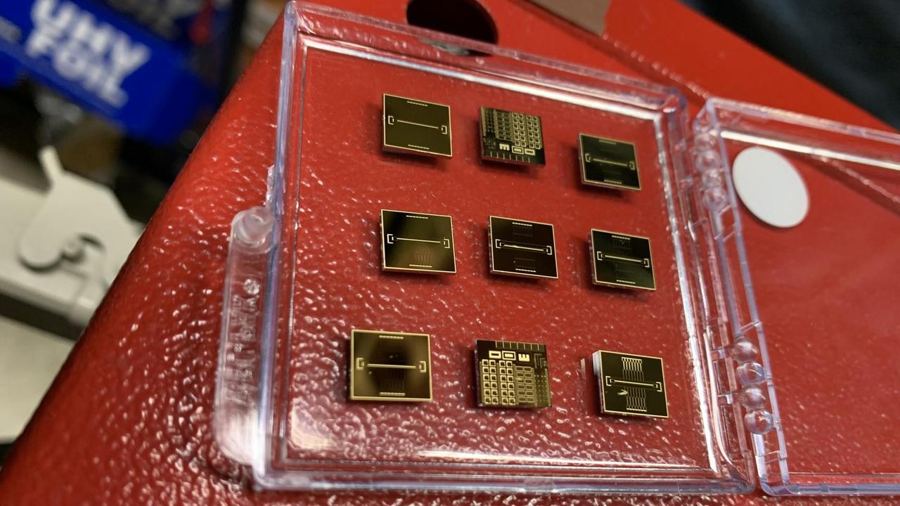 Neun goldmetallische Ionenfallen-Chips liegen in einem aufgeklappten Plastikcover Neun goldmetallische Ionenfallen-Chips liegen in einem aufgeklappten Plastikcover