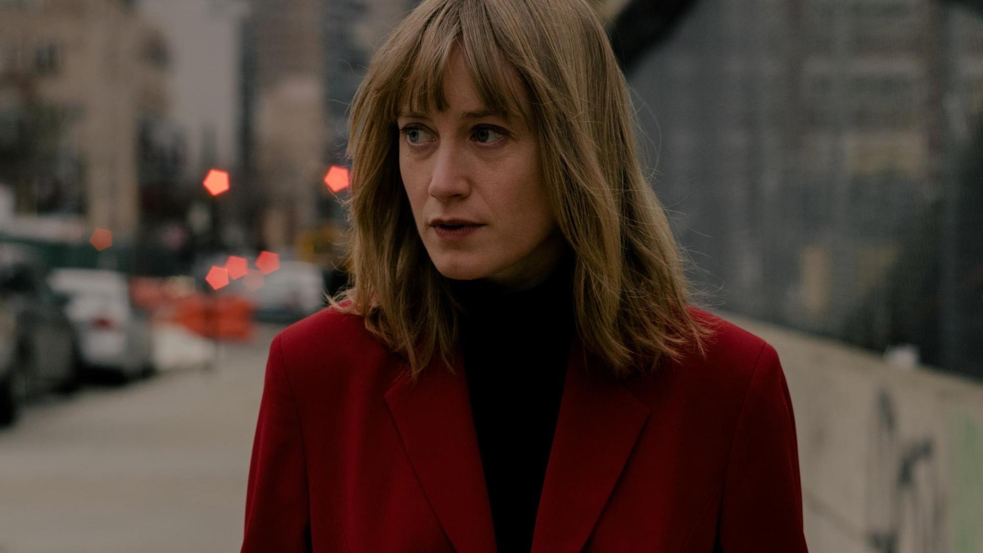 Tamara Lindeman trägt einen roten Mantel, im Hintergrund eine Großstadt