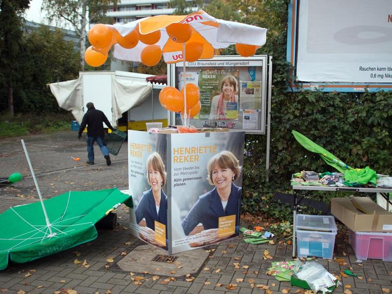 Wahlkampfmaterial und ein umgeworfener Schirm liegen vor dem Tatort, dem Stand von Henriette Reker.