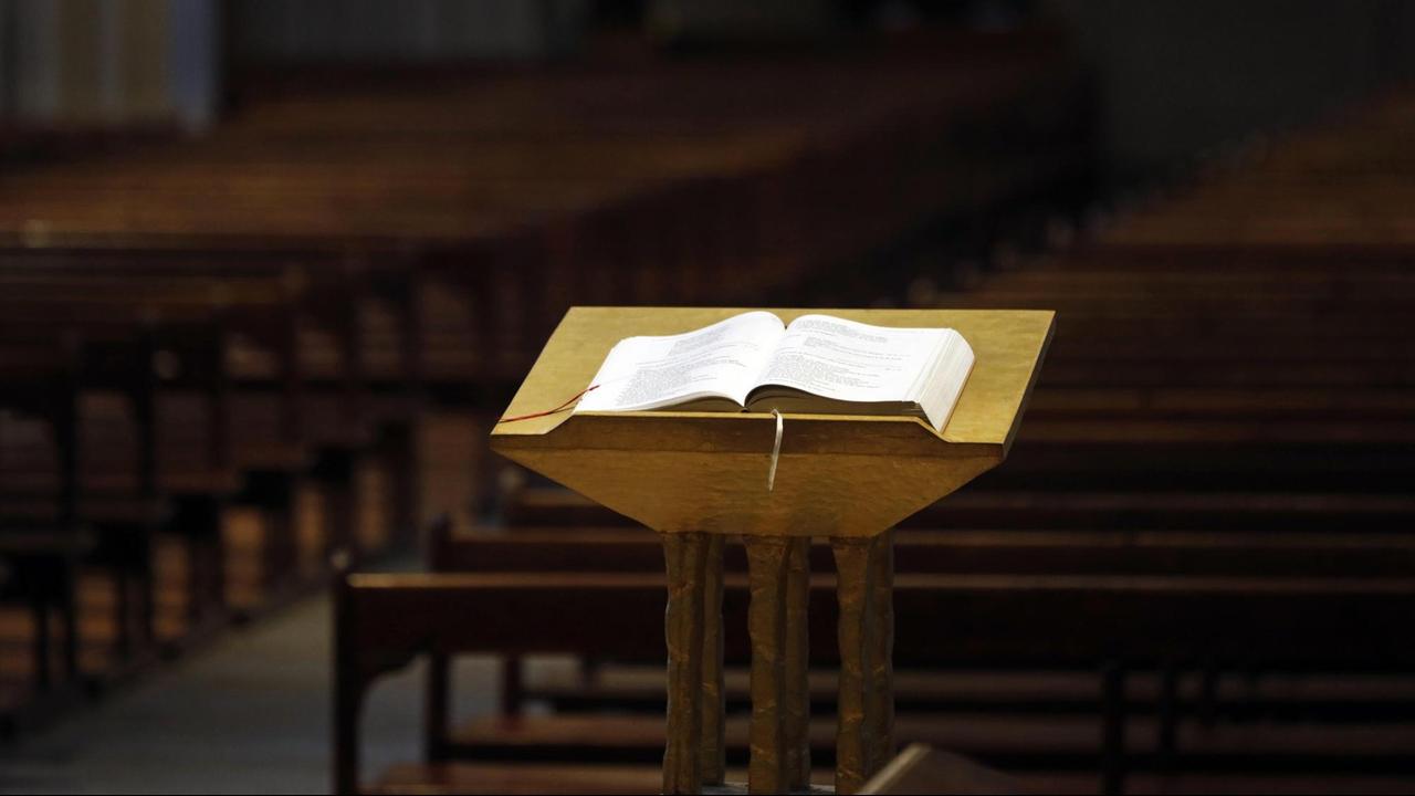 Eine Kirche im Lockdown. Eine aufgeschlagene Bibel auf einem Stehpult vor leeren Kirchenbänken. Eine Kirche im Lockdown. Eine aufgeschlagene Bibel auf einem Stehpult vor leeren Kirchenbänken.