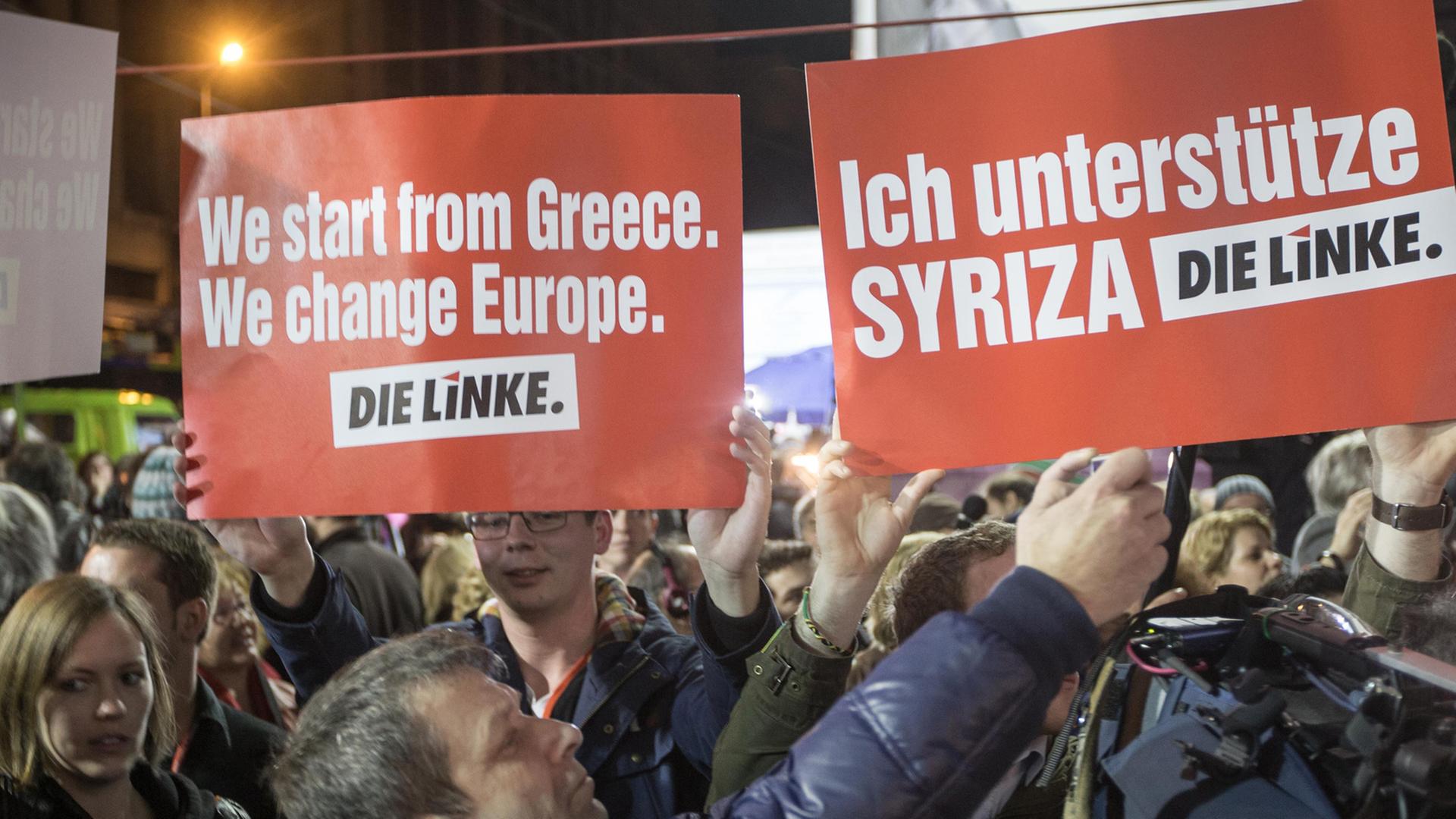In einer Menschenmenge halten Griechen zwei Schilder der Linkspartei hoch, auf denen u.a. steht: "Ich unterstütze Syriza". In einer Menschenmenge halten Griechen zwei Schilder der Linkspartei hoch, auf denen u.a. steht: "Ich unterstütze Syriza".