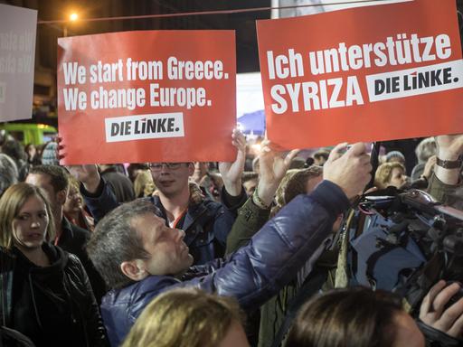 In einer Menschenmenge halten Griechen zwei Schilder der Linkspartei hoch, auf denen u.a. steht: "Ich unterstütze Syriza".