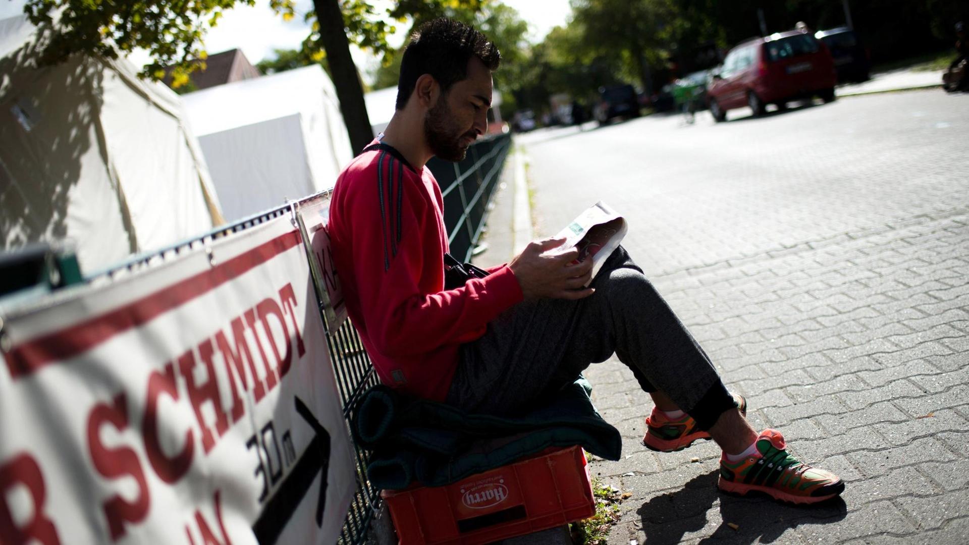 Ein Mann sitzt am 09.09.2015 auf einem Weg auf dem Gelände der Flüchtlingsunterkunft in der ehemaligen Schmidt-Knobelsdorf-Kaserne in Berlin und liest Zeitung.