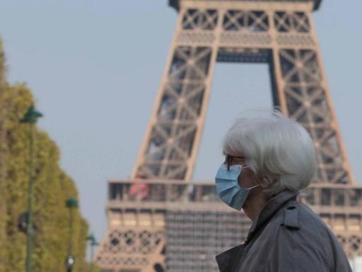Eine Frau mit Mund-Nase-Schutz vor dem Pariser Eiffelturm