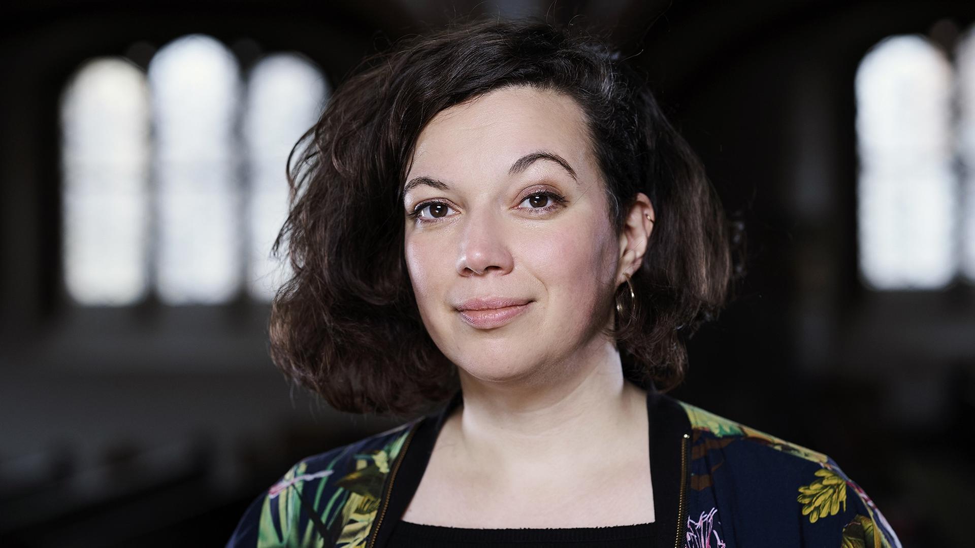 Die Pastorin Jasmin El-Manhy steht in einer Kirche und schaut in die Kamera. Im Hintergrund sind die Kirchenfenster zu sehen. Die Pastorin Jasmin El-Manhy steht in einer Kirche und schaut in die Kamera. Im Hintergrund sind die Kirchenfenster zu sehen.