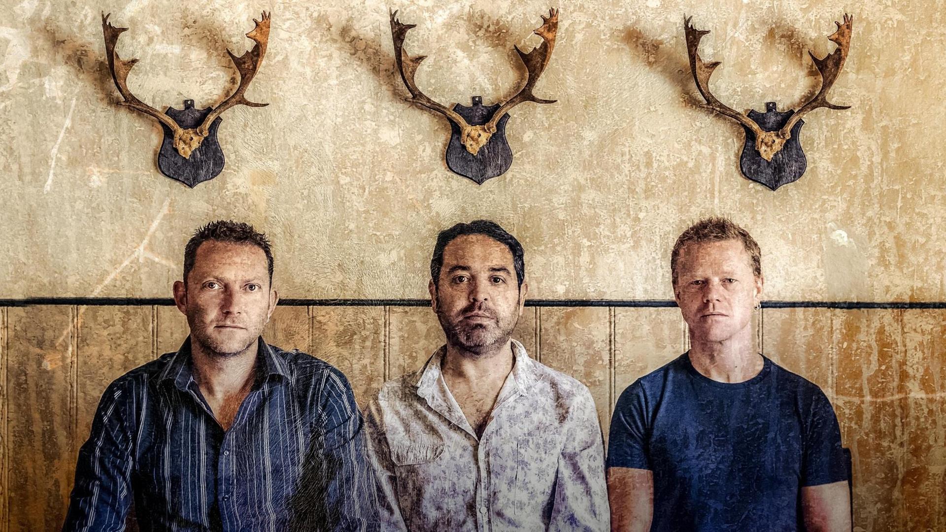 Die drei Musiker der Band Faustus sitzen unter drei kleinen Hirschgeweihen Die drei Musiker der Band Faustus sitzen unter drei kleinen Hirschgeweihen