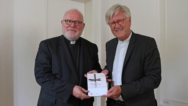 Kardinal Reinhard Marx und der EKD Ratsvorsitzende Heinrich Bedford-Strohm halten gemeinsam das Wort zum Jahr 2017 in die Höhe.