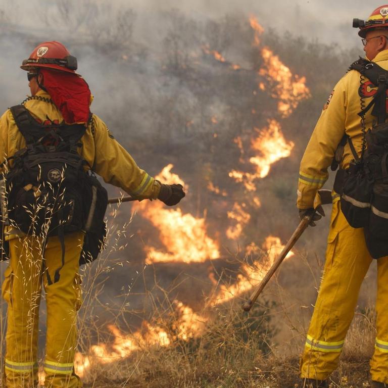 Feuerwehrmänner in Santa Clarita blicken auf ein Tal hinab, in dem die Brände noch wüten.