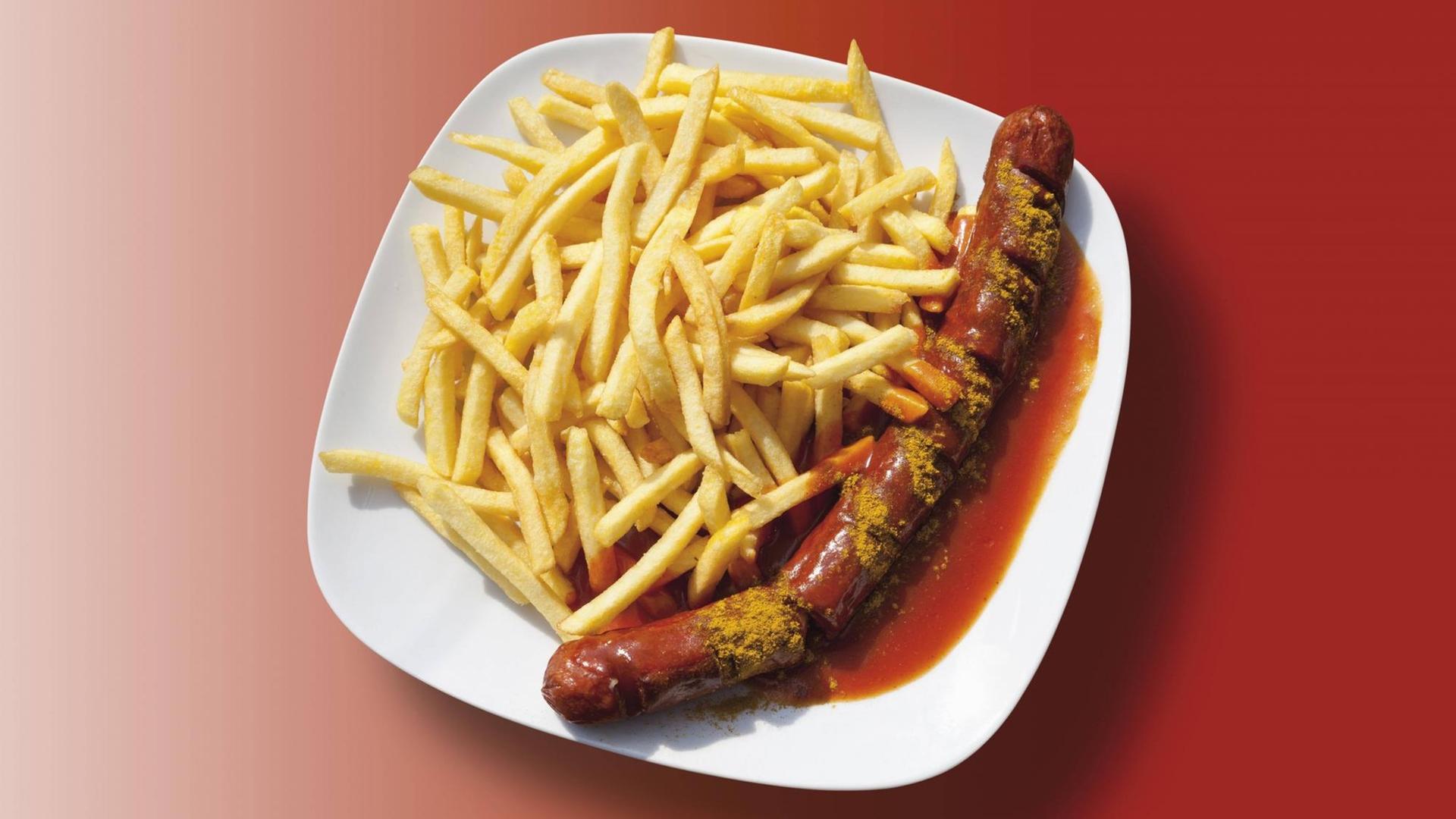 Nahaufnahme eines angerichteten Tellers mit Currywurst, Pommes und Sauße auf einem Untergrund mit rotem Verlauf. Nahaufnahme eines angerichteten Tellers mit Currywurst, Pommes und Sauße auf einem Untergrund mit rotem Verlauf.