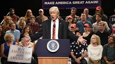 Alec Baldwin steht in seiner Rolle als Donald Trump verkleidet an einem Redepult.