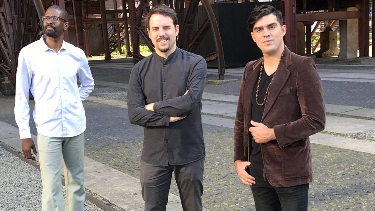 Daniel Garcia Trio stehen in einer Industrieanlage Daniel Garcia Trio stehen in einer Industrieanlage