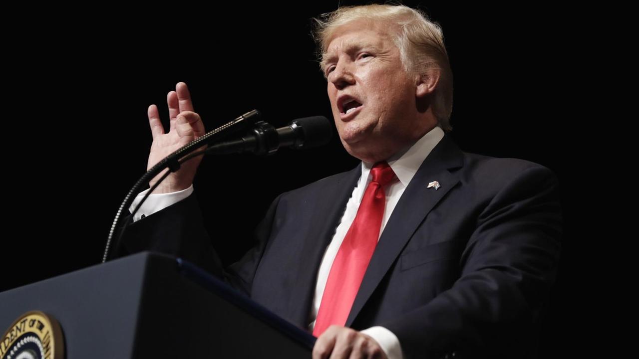 Trump steht vor schwarzem Hintergrund an einem Rednerpult, spricht und gestikuliert mit der rechten Hand. Trump steht vor schwarzem Hintergrund an einem Rednerpult, spricht und gestikuliert mit der rechten Hand.