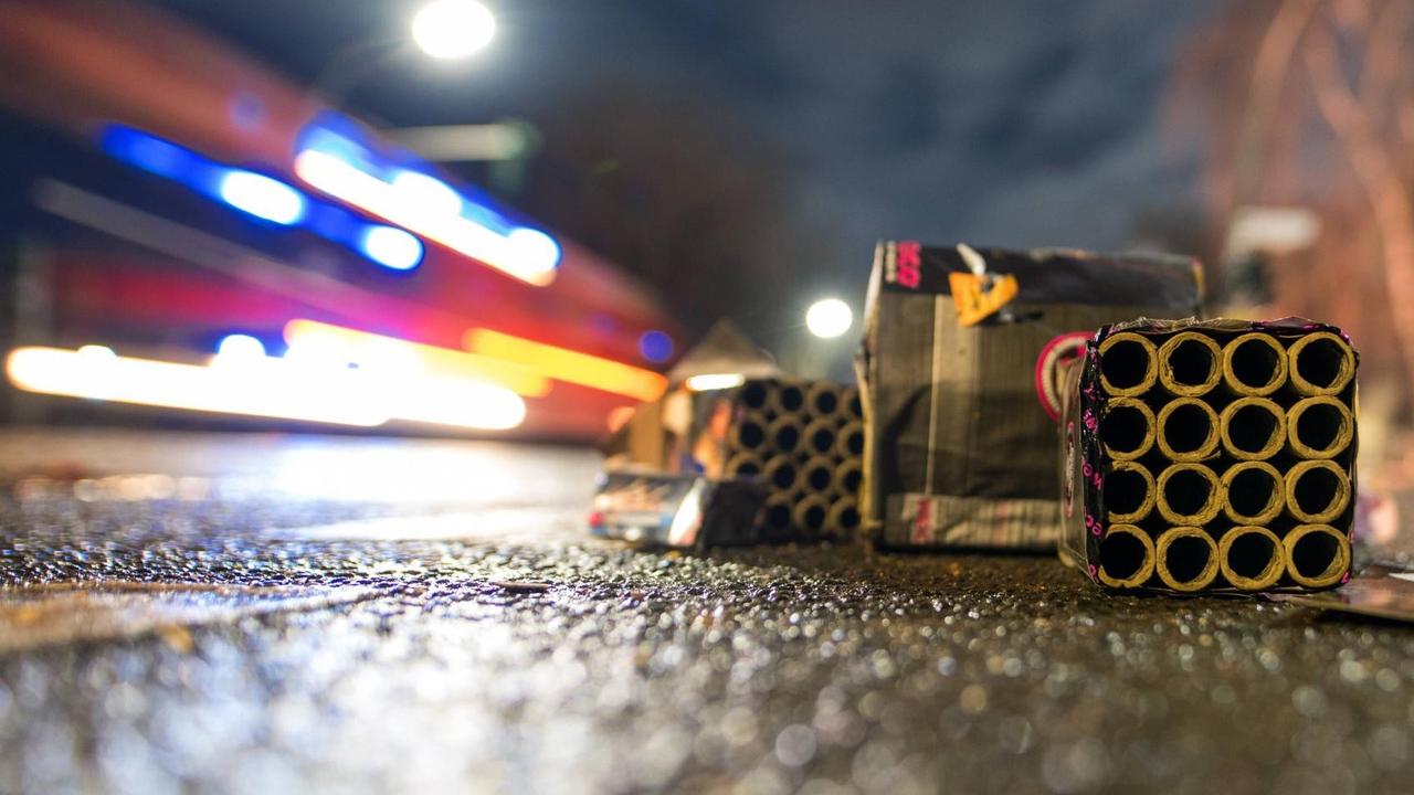 Zu sehen sind im Vordergrund Silvester-Böller, im Hintergrund verschwommen ein Feuerwehrfahrzeug. Zu sehen sind im Vordergrund Silvester-Böller, im Hintergrund verschwommen ein Feuerwehrfahrzeug.