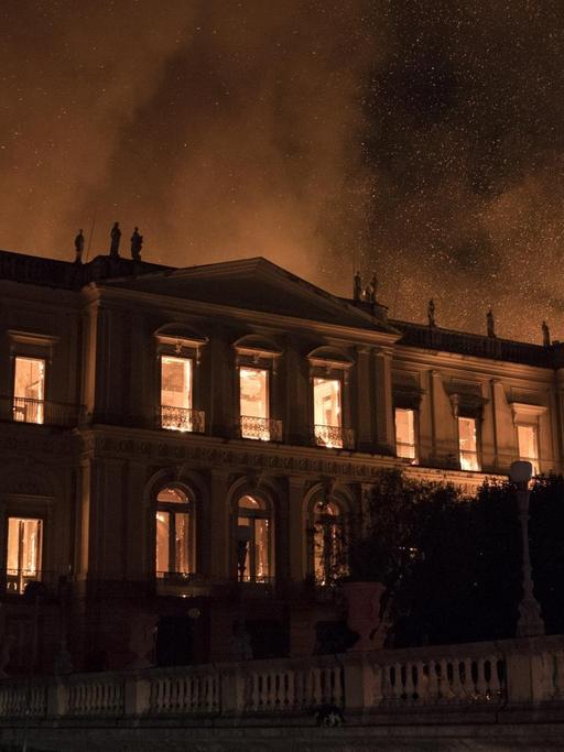 Das Bild zeigt das brennende Gebäude des Nationalmuseums in der Nacht, durch die Fenster sieht man die Flammen, Rauch und Funken steigen in den Nachthimmel.
