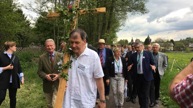 Ein Mann trägt ein Holz-Kreuz auf der Schulter. Hinter ihm läuft eine Wandergruppe. Die Gruppe pilgert auf dem neuen Lutherweg in Hessen. Foto: Deutschlandradio/Ludger Fittkau