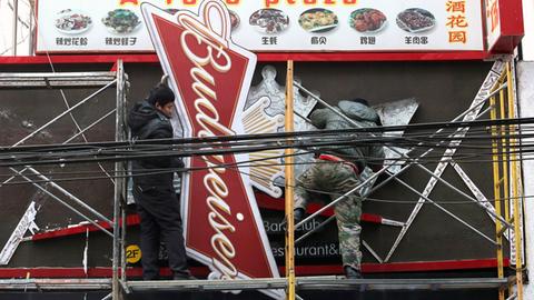 Arbeiter montieren ein "Budweiser"-Werbeschild an einem Restaurant ab.