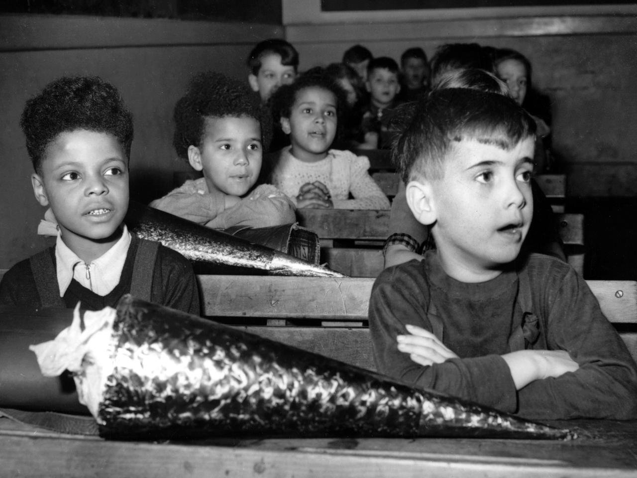 Erstklässler, darunter mehrere Besatzungskinder, sitzen an ihrem ersten Schultag im Klassenzimmer.