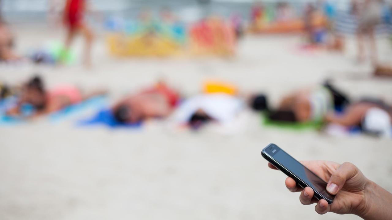 Eine Frau schreibt am 04.08.2013 mit einem Mobiltelefon eine SMS am Strand von Kolberg, Polen, an der Ostsee. Eine Frau schreibt am 04.08.2013 mit einem Mobiltelefon eine SMS am Strand von Kolberg, Polen, an der Ostsee.