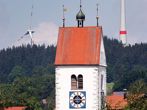 Der Turm der Pfarrkirche von Wildpoldsried im Allgäu. Im Hintergrund: Ein Windrad