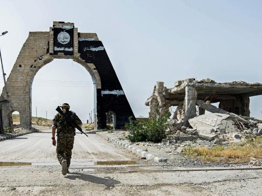 Ein kurdischer Kämpfer nähert sich einem Tor in der Nähe des Tischrin-Dammes in der syrischen Provinz Aleppo, auf dem das Logo des IS prangt, der von dort vertrieben wurde