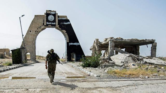 Ein kurdischer Kämpfer nähert sich einem Tor in der Nähe des Tischrin-Dammes in der syrischen Provinz Aleppo, auf dem das Logo des IS prangt, der von dort vertrieben wurde