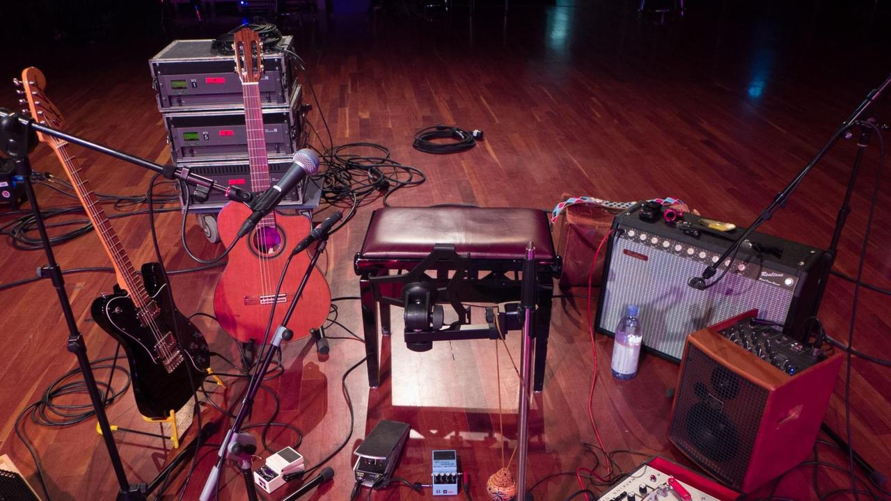Eine E- und eine akustische Gitarre in Ständern, daneben ein Hocker, Kabel und ein Gitarrenverstärker. Eine E- und eine akustische Gitarre in Ständern, daneben ein Hocker, Kabel und ein Gitarrenverstärker.