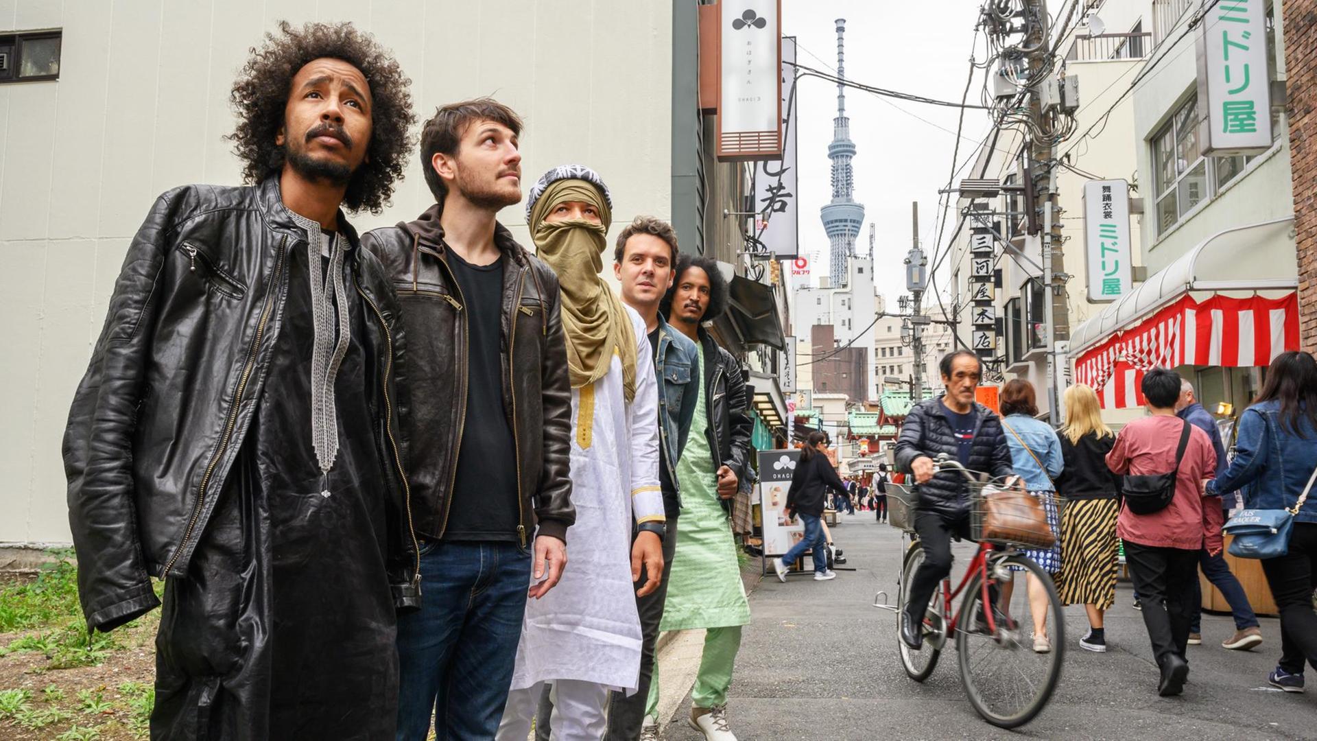 Fünf Männer stehen hintereinander an einer Strasse in Asien. Zwei Männer haben traditionelle Kleidung der Tuareg an. Fünf Männer stehen hintereinander an einer Strasse in Asien. Zwei Männer haben traditionelle Kleidung der Tuareg an.