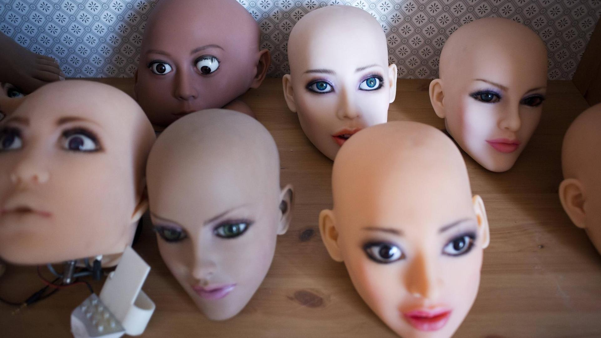 Weiblich aussehende Köpfe von Sexrobotern mit künstlicher Intelligenz stehen auf einer Holzfläche. Weiblich aussehende Köpfe von Sexrobotern mit künstlicher Intelligenz stehen auf einer Holzfläche.