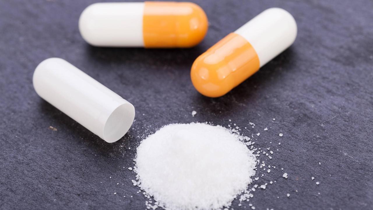 Weiß-orangefarbene Pillen und weißes Pulver auf schwarzem Hintergrund. Weiß-orangefarbene Pillen und weißes Pulver auf schwarzem Hintergrund.