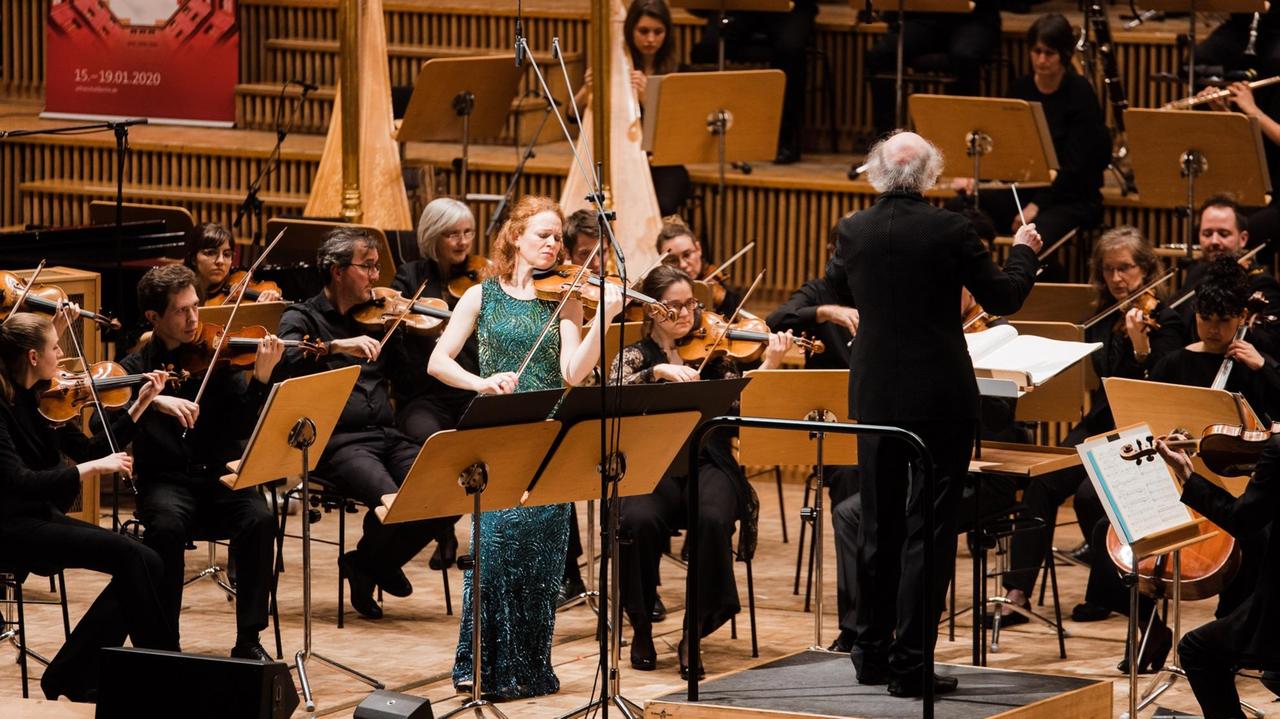 Die Geigerin steht neben dem Dirigenten nahe des Orchesters Die Geigerin steht neben dem Dirigenten nahe des Orchesters