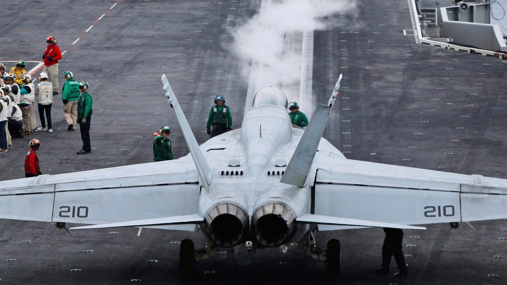 Auf dem Flugzeugträger "USS Ronald Reagan" steht ein Kampfjet, daneben sind einige Menschen zu sehen. Auf dem Flugzeugträger "USS Ronald Reagan" steht ein Kampfjet, daneben sind einige Menschen zu sehen.