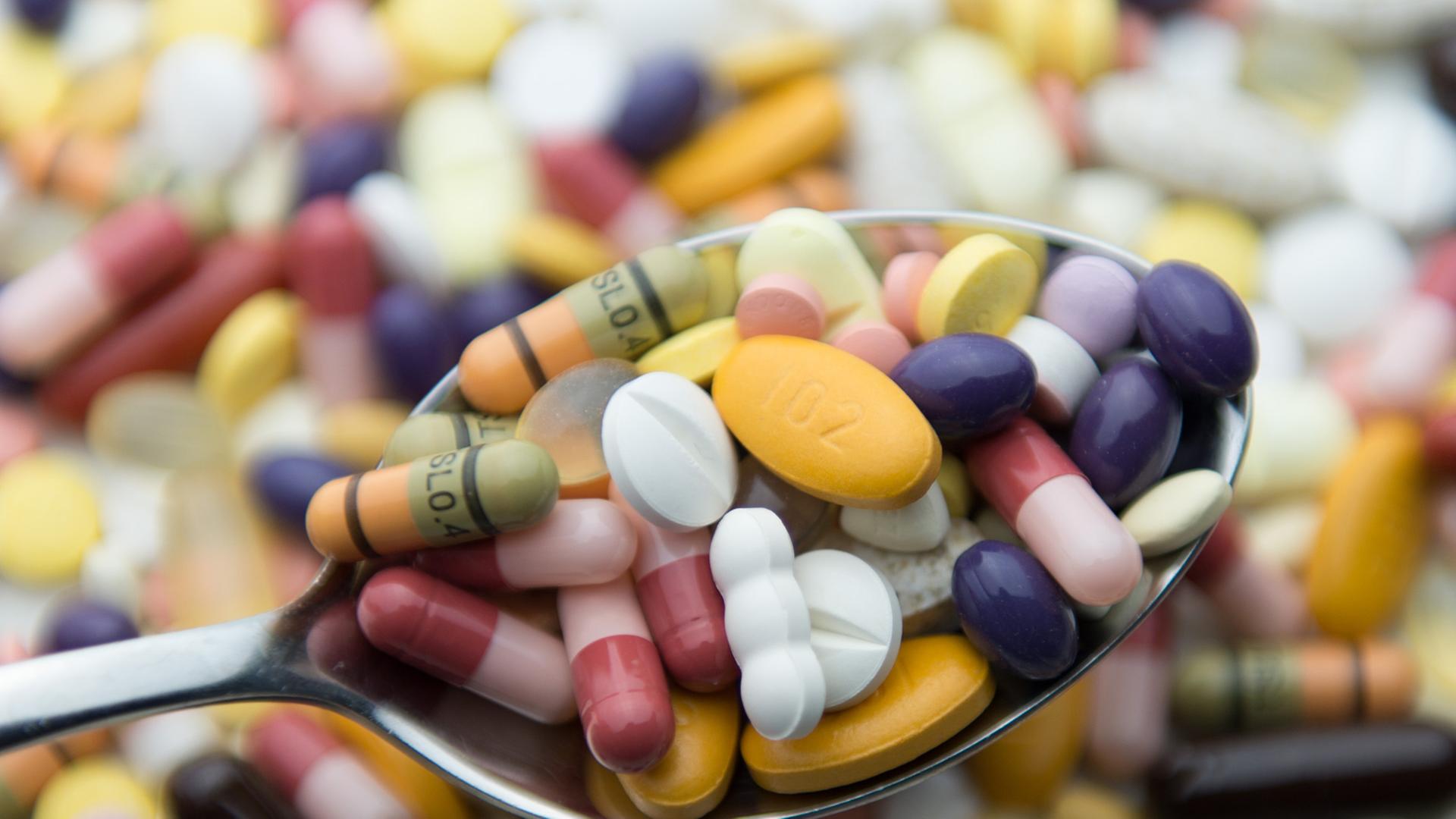 Zahlreiche Pillen und Tabletten liegen auf einem Tisch und auf einem Löffel. Zahlreiche Pillen und Tabletten liegen auf einem Tisch und auf einem Löffel.
