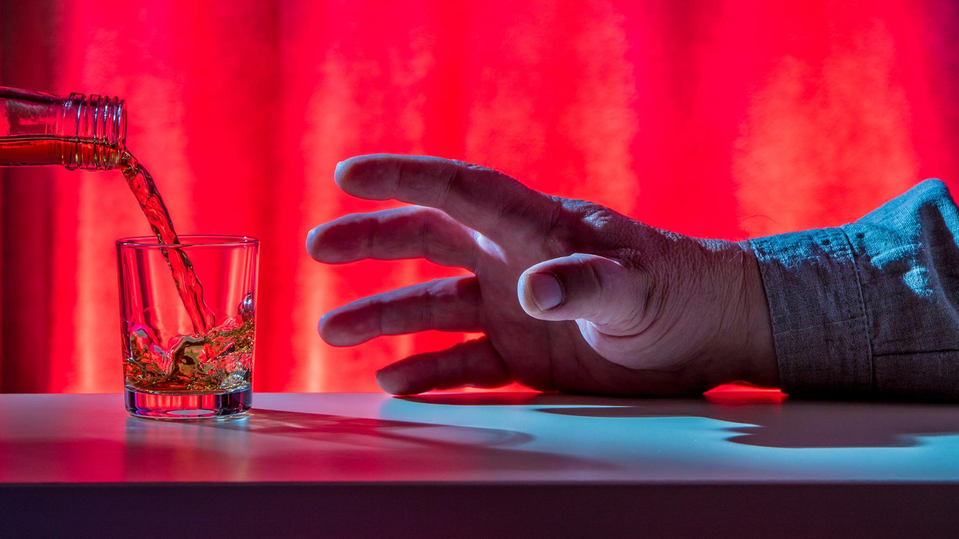 Eine Hand greift nach einem Schnapsglas. Eine Hand greift nach einem Schnapsglas.