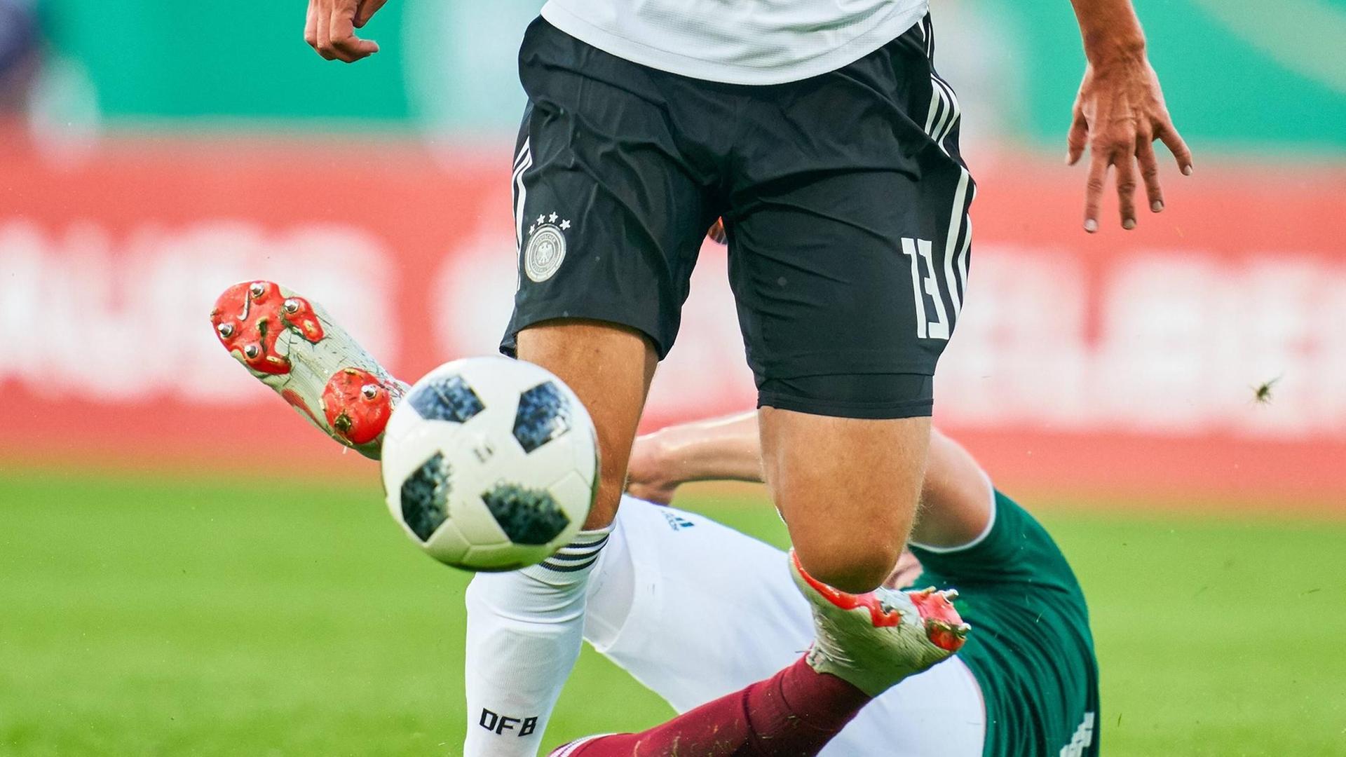 Ein deutscher U21-Spieler im Duell gegen einen mexikanischen Gegner, der am Boden liegt. Zu sehen sind nur die Beine der Spieler und der Ball.