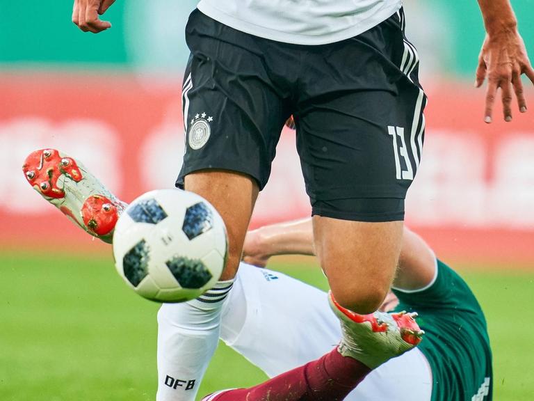 Ein deutscher U21-Spieler im Duell gegen einen mexikanischen Gegner, der am Boden liegt. Zu sehen sind nur die Beine der Spieler und der Ball.