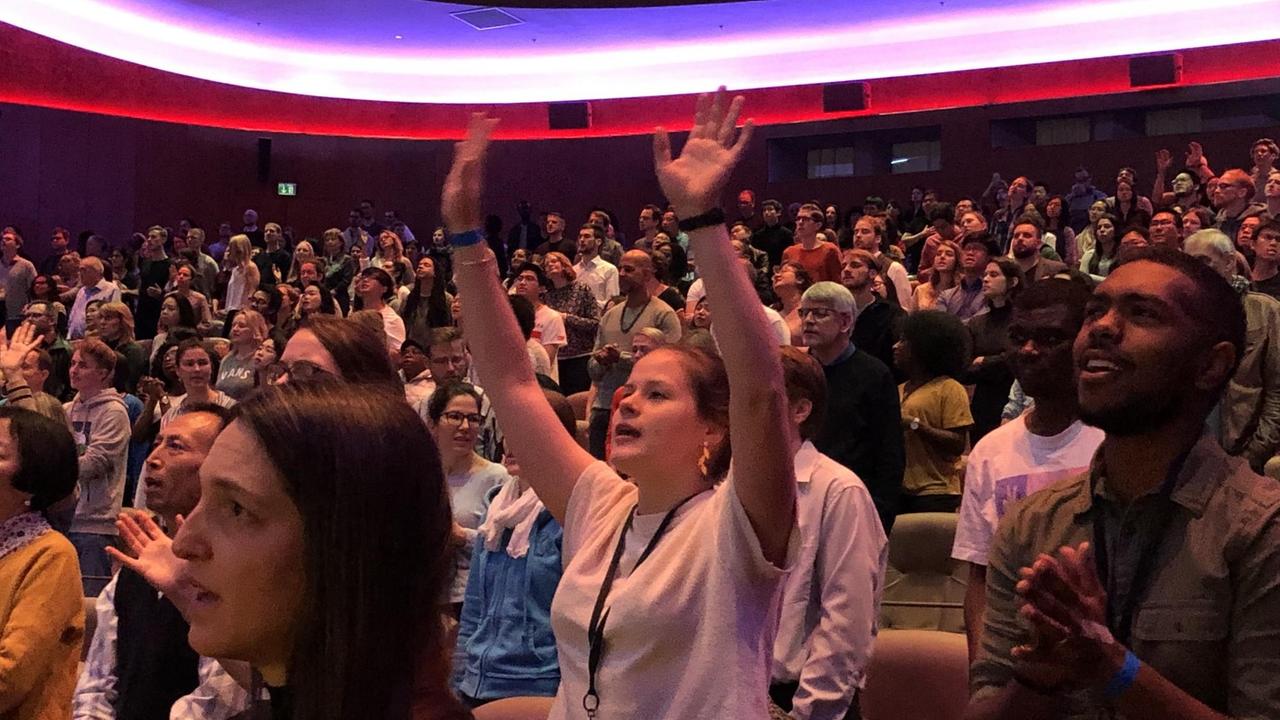 Blick auf die Teilnehmer des Saddleback-Gottesdienstes im Zoopalast Berlin, eine junge Frau reckt die Hände in die Luft.