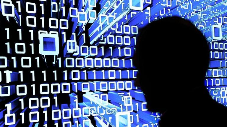 Ein Mensch geht an einem Leuchtdisplay vorbei und wird mit Binärcode beleuchtet Ein Mensch geht an einem Leuchtdisplay vorbei und wird mit Binärcode beleuchtet