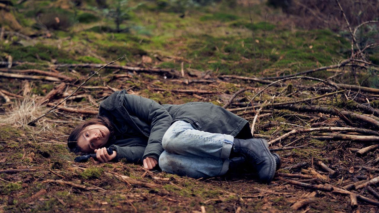 Szene aus der Serie "Unbroken": Alex (Aylin Tezel) ist völlig am Ende und liegt zusammengekauert auf dem Waldboden. 