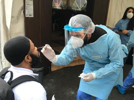 Ein Helfer führt einer Person einen Teststab in die Nase ein