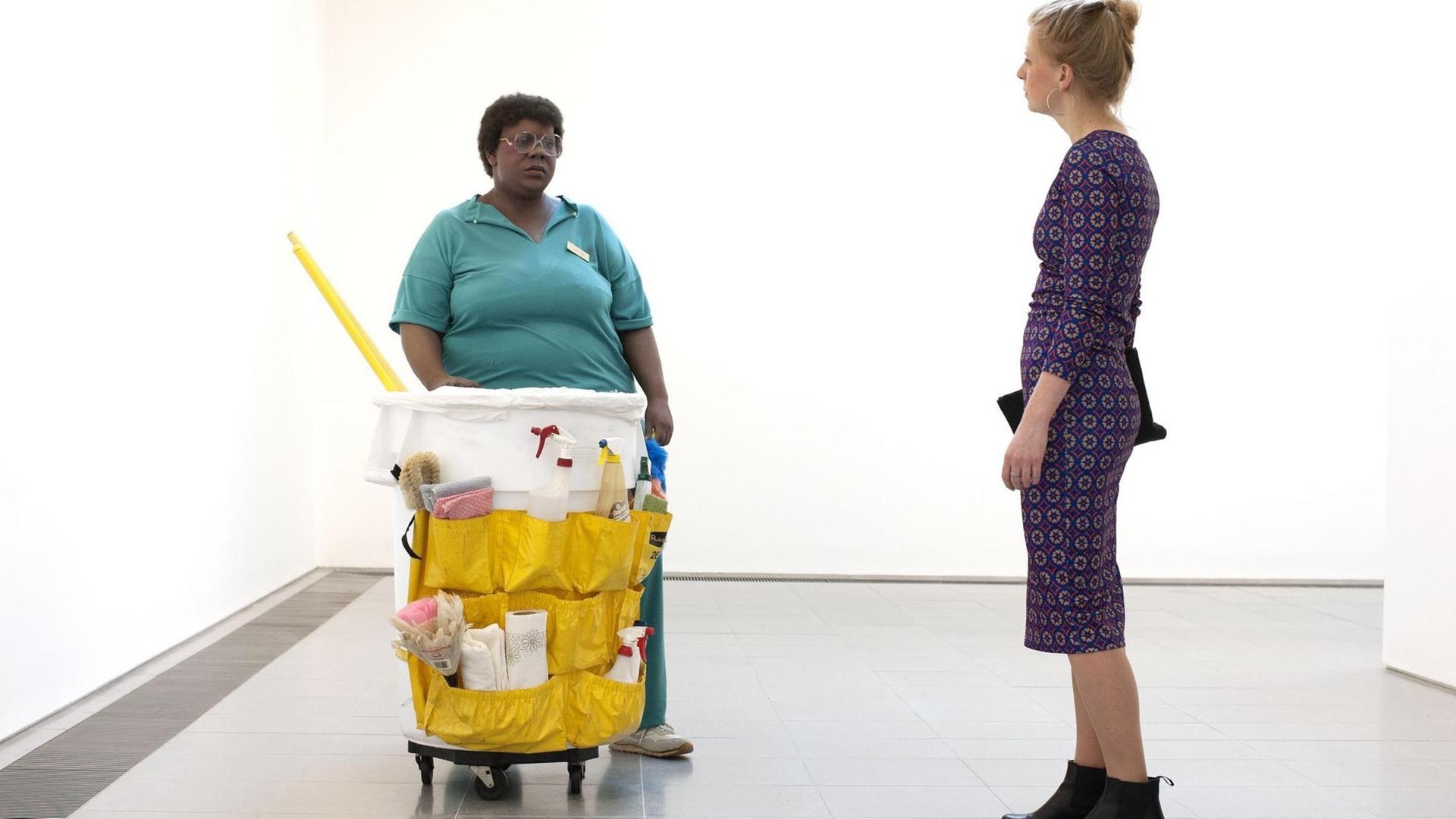 Ein Farbfoto zeigt eine Besucherin in derSerpentine Sackler Gallery in London beim Betrachten der Skulptur ç Die lebensechte Darstellung einer afroamerikanischen Reinigungskraft mit Besen und einem Wagen voller Reinigungsmittel und und Wäschewagen zu sehen ist und einer Serpentine Galleries' Summer Exhibitions. Ein Farbfoto zeigt eine Besucherin in derSerpentine Sackler Gallery in London beim Betrachten der Skulptur ç Die lebensechte Darstellung einer afroamerikanischen Reinigungskraft mit Besen und einem Wagen voller Reinigungsmittel und und Wäschewagen zu sehen ist und einer Serpentine Galleries' Summer Exhibitions.
